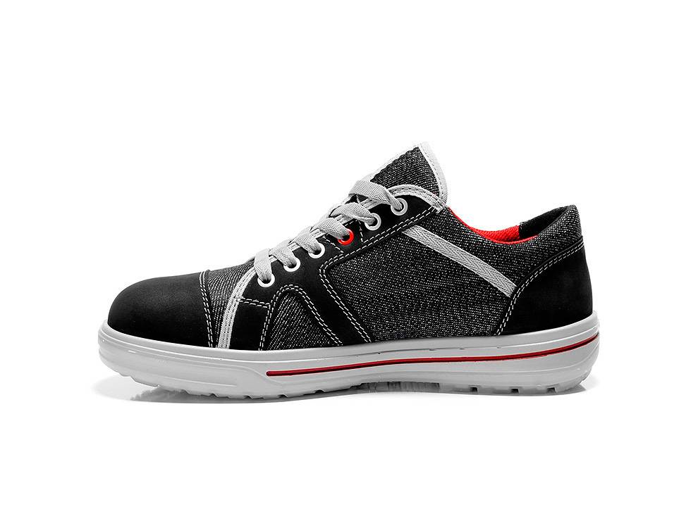 Ein schwarzer und grauer Sneaker mit weißen Schnürsenkeln und roten Innenflächen. Der Schuh hat weiße Nähte und eine weiße Sohle mit einem roten Streifen.