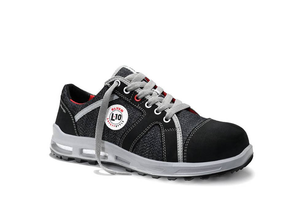 Ein schwarzer und grauer Sportschuh mit roten Innenakzenten und weißen Schnürsenkeln. Der Schuh verfügt über einen kreisförmigen Emblem an der Seite mit der Aufschrift 