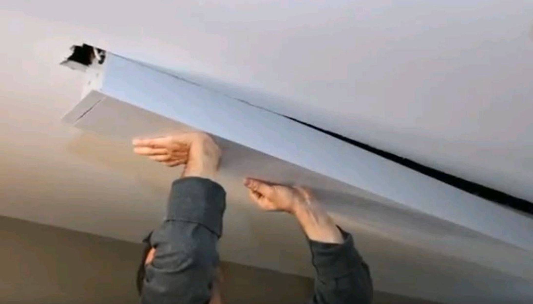 Eine Person, die eine lange Deckenleuchte oder Abdeckung hebt, während sie darunter in einem Innenraum steht.