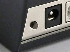 Nahaufnahme eines Metallgerätepanels mit einem runden Anschluss, einem kleinen Knopf und einer dunklen Buchsenöffnung.