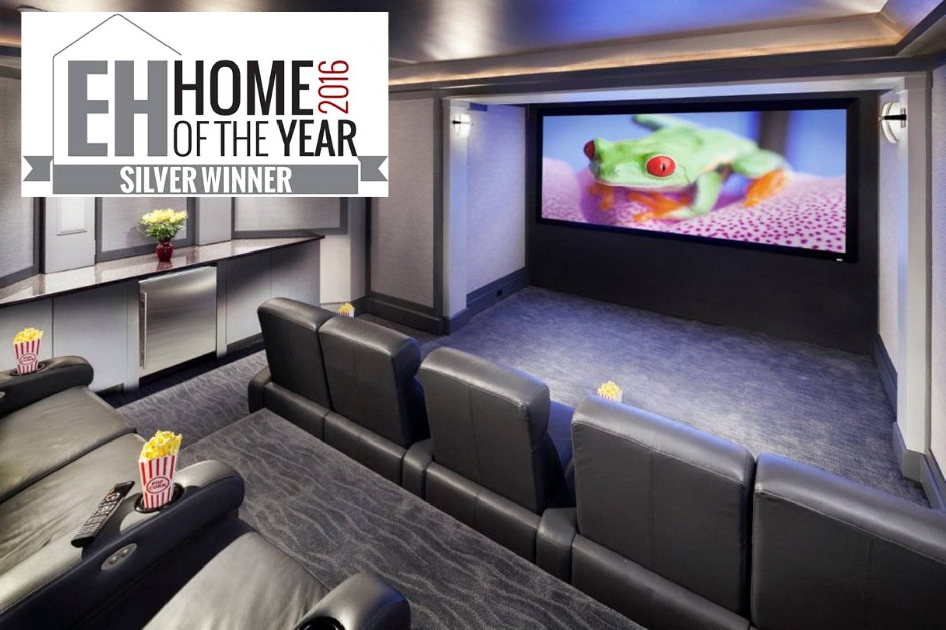 Modernes Heimkino mit Reihen schwarzer Liegestühle, die auf einen großen Wandbildschirm ausgerichtet sind; Banner „EH Home of the Year 2016 Silver Winner" in der oberen linken Ecke.