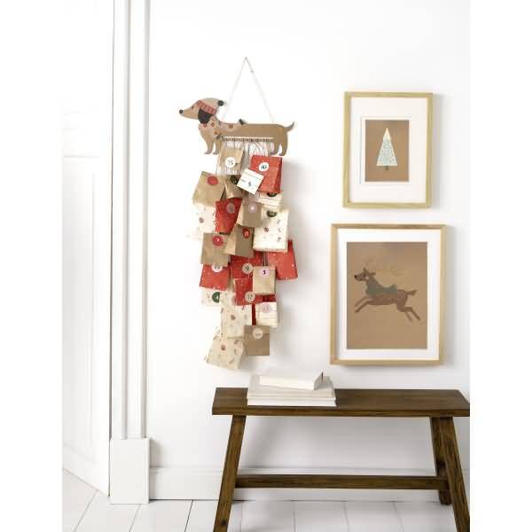 Wandmontierte Weihnachts-Countdown-Anzeige mit nummerierten Stoffbeuteln, neben Rahmenkunst über einer hölzernen Bank.
