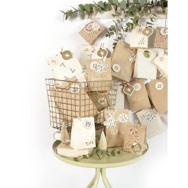 Eine dekorative Adventskalender-Ausstellung mit nummerierten Papiertüten und Tags, die auf einem kleinen Tisch und in einem Drahtkorb angeordnet sind, mit Eukalyptus-Grün darüber.