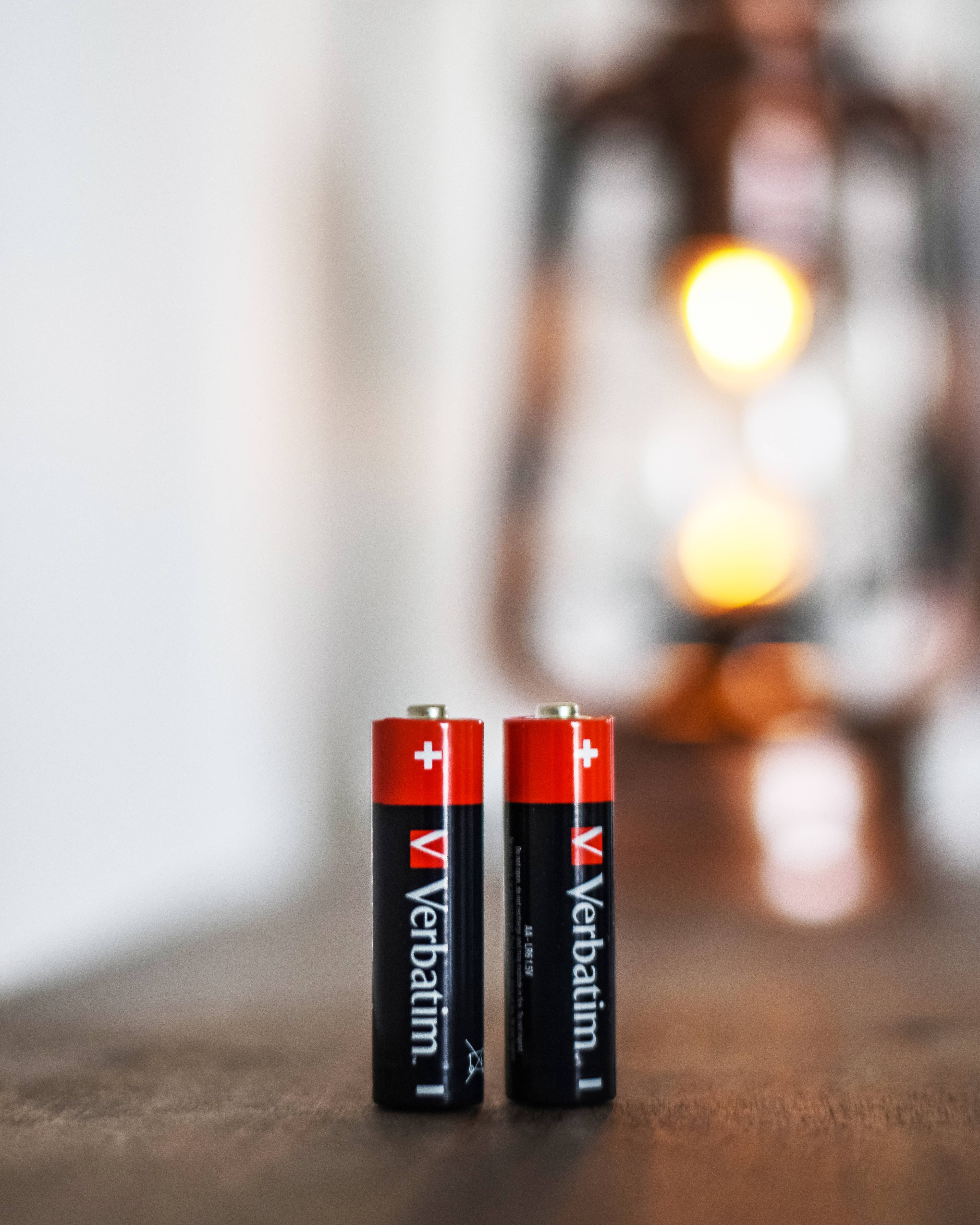 Zwei aufrecht auf einem Tisch stehende Verbatim-AAA-Batterien mit einer unscharfen Lampe im Hintergrund.