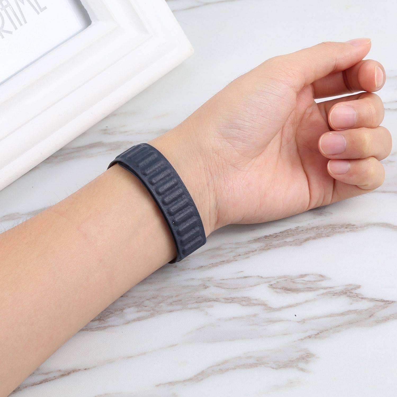 Nahaufnahme eines Handgelenks, das ein schwarzes Fitness-Armband auf einer hellen Marmoroberfläche trägt.