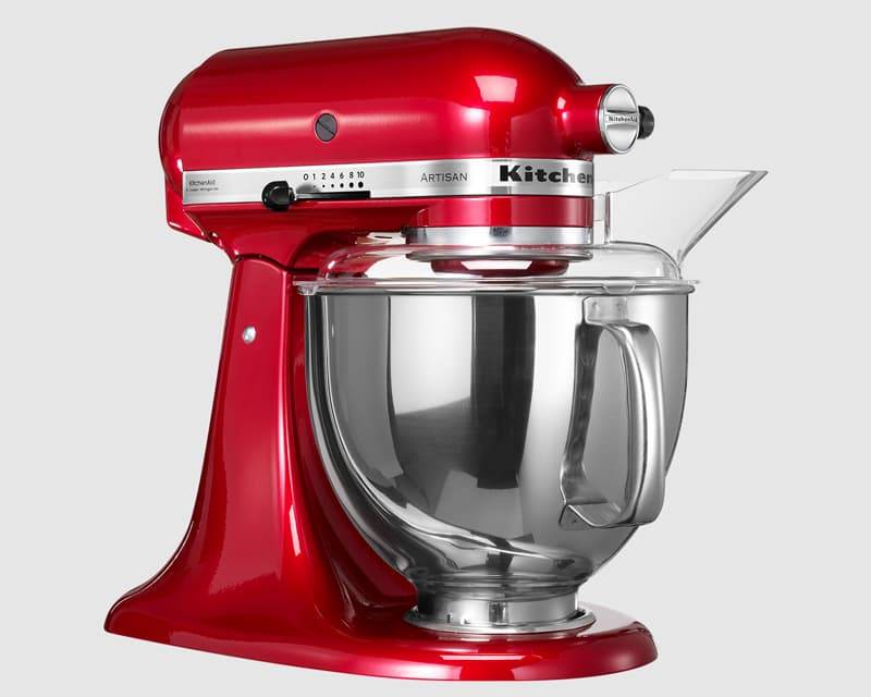 Roter KitchenAid Artisan Standmixer mit Edelstahlschüssel und transparentem Ausgießschutz, in Seitenansicht auf einfachem Hintergrund dargestellt.