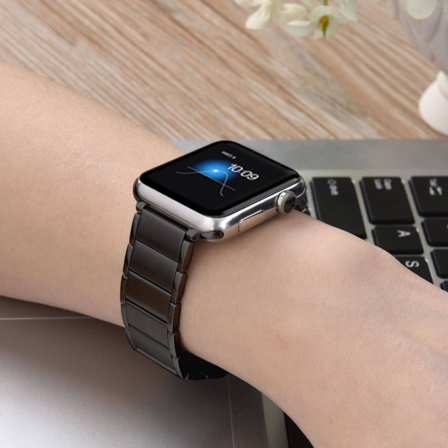 Nahaufnahme einer Smartwatch mit schwarzem Metallband am Handgelenk einer Person neben einer Laptop-Tastatur.