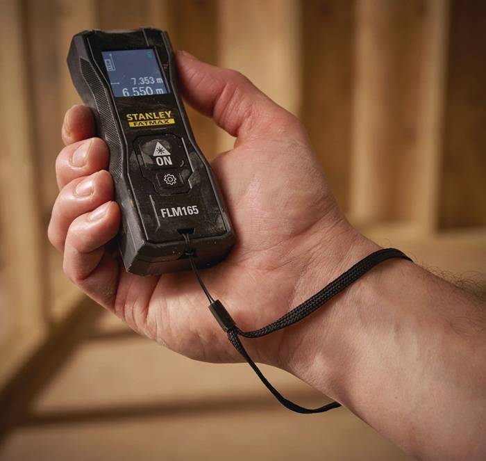 Eine Hand, die einen Stanley Laserentfernungsmesser hält und eine Entfernungsanzeige in einer Holzbaustelle zeigt.