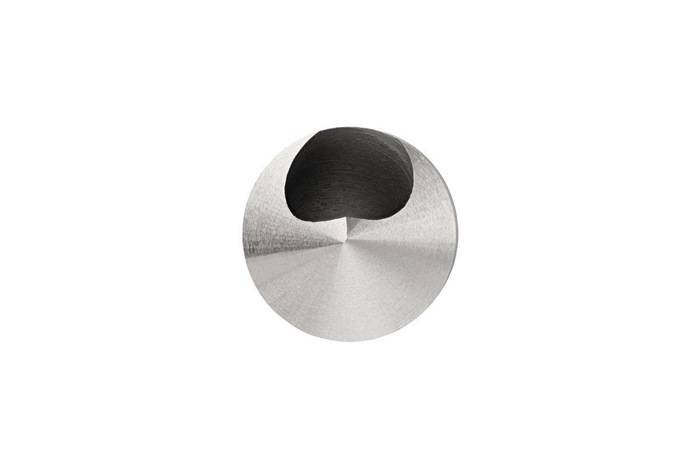 Das Bild zeigt die Spitze eines hohlen Metallinstruments mit einer kreisrunden Öffnung, höchstwahrscheinlich eine Rohrleitung oder Düse, von vorne gegen einen weißen Hintergrund betrachtet.