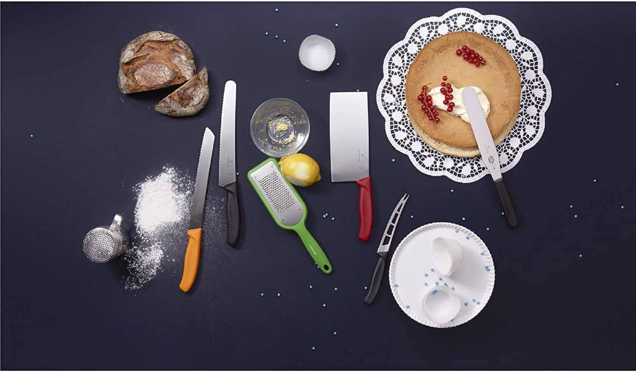 Overhead-Backansicht mit Mehl, Brotlaib, Zitrone, Reibe, Messern, Messbechern, Rührschüssel und einem Biskuitkuchen mit Creme und roten Beeren