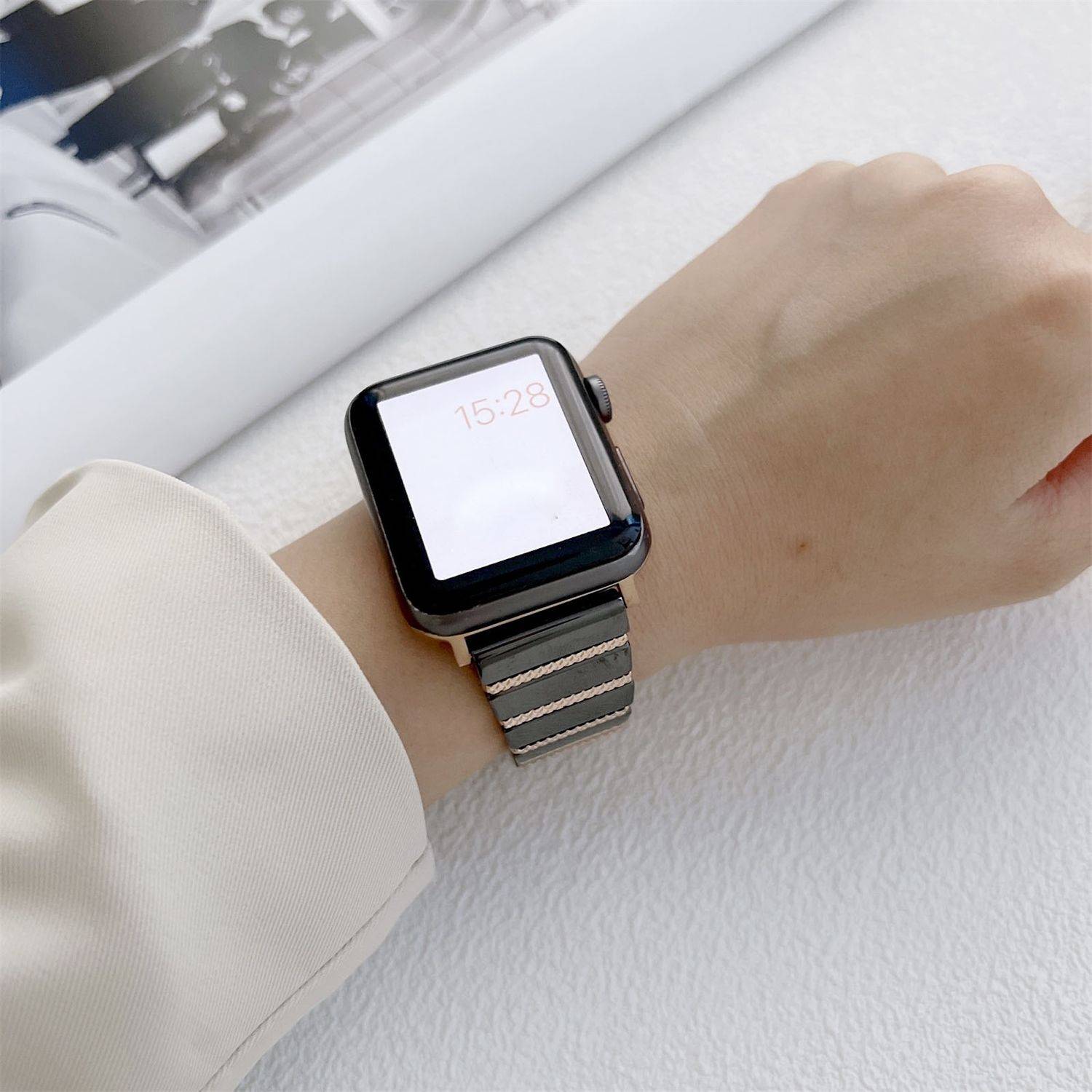 Eine schwarze Smartwatch mit Metallarmband, getragen am Handgelenk einer Person, zeigt die Uhrzeit 15:28.