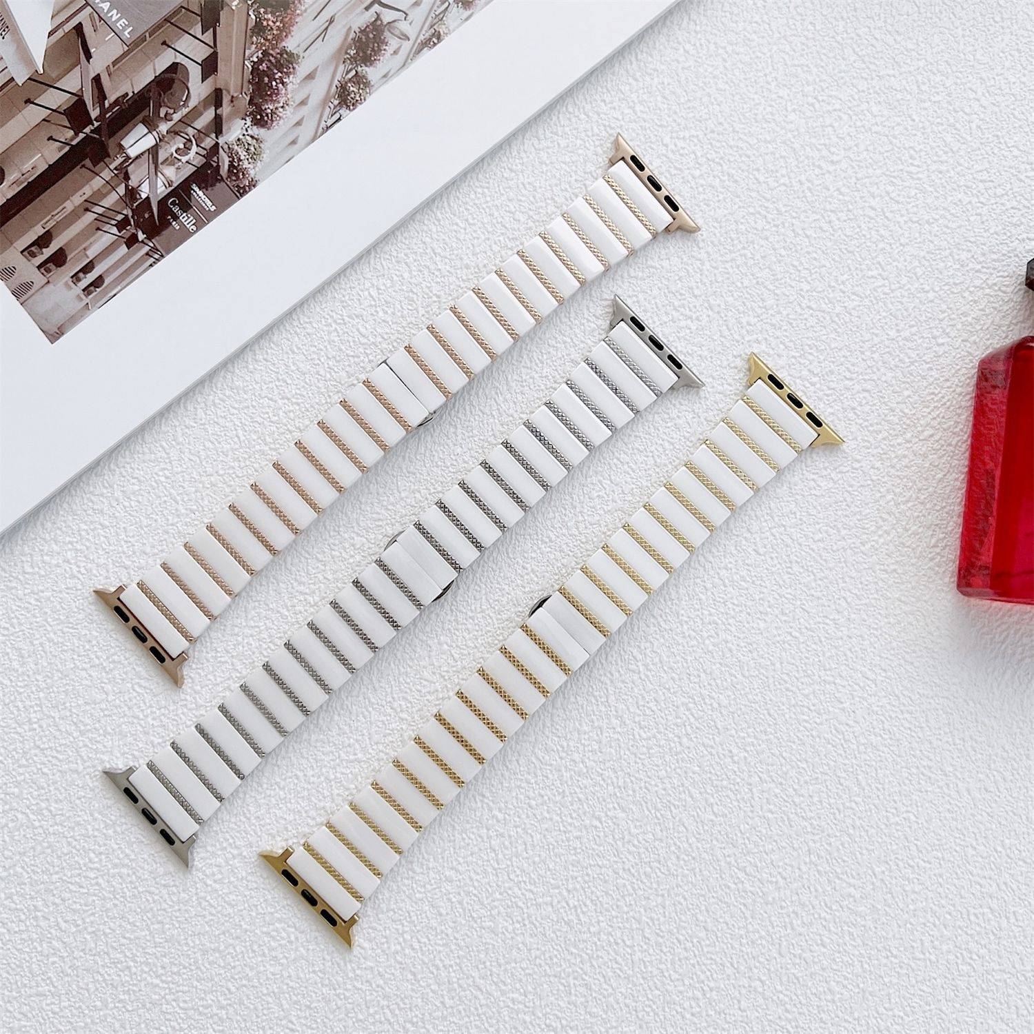 Drei austauschbare Uhrenarmbänder in weiß-, silber- und goldgestreiften Designs diagonal auf einer hellen Oberfläche angeordnet.