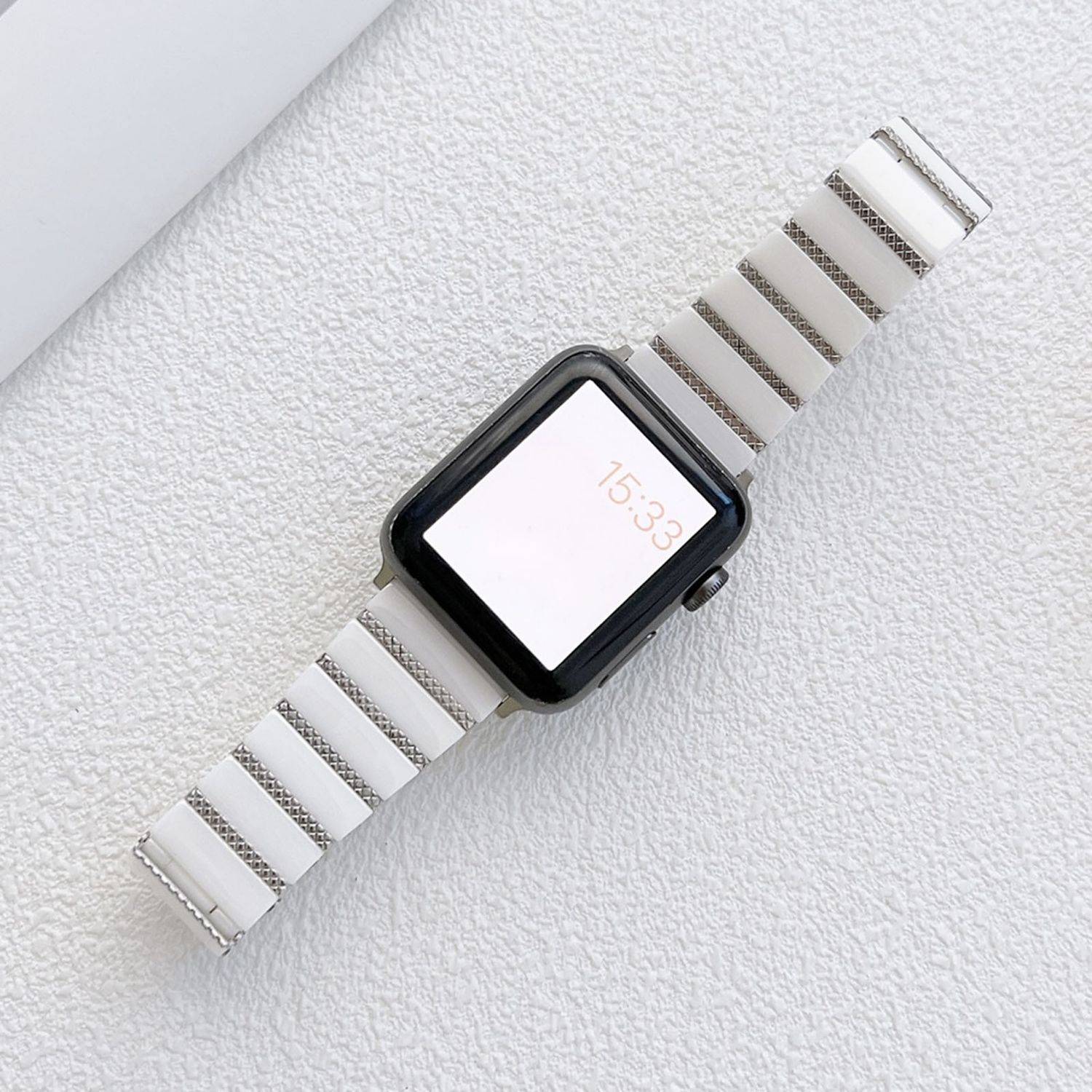 Smartwatch mit schwarzem Gehäuse und weiß gestreiftem Armband, das die Uhrzeit 15:33 auf einem hell strukturierten Hintergrund anzeigt.