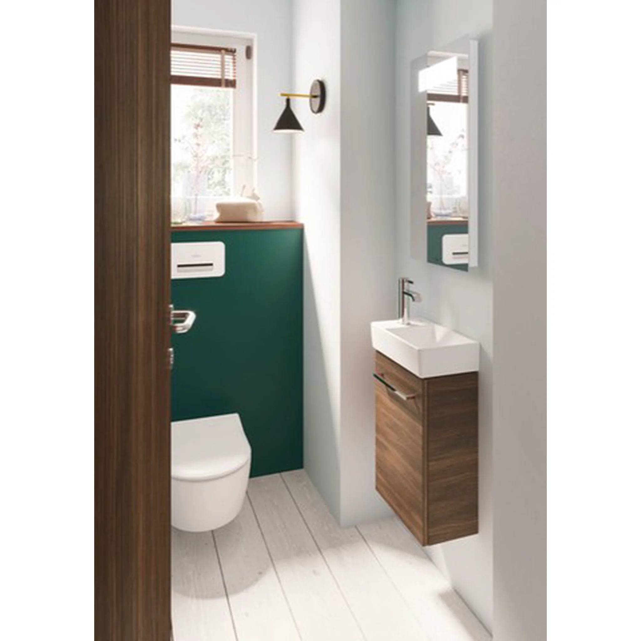 Kompaktes modernes Badezimmer mit Toilette, wandmontiertem Waschbecken, Spiegel und Fenster, ausgestattet mit weißen Wänden, Holzakzenten und einer grünen Rückwand.