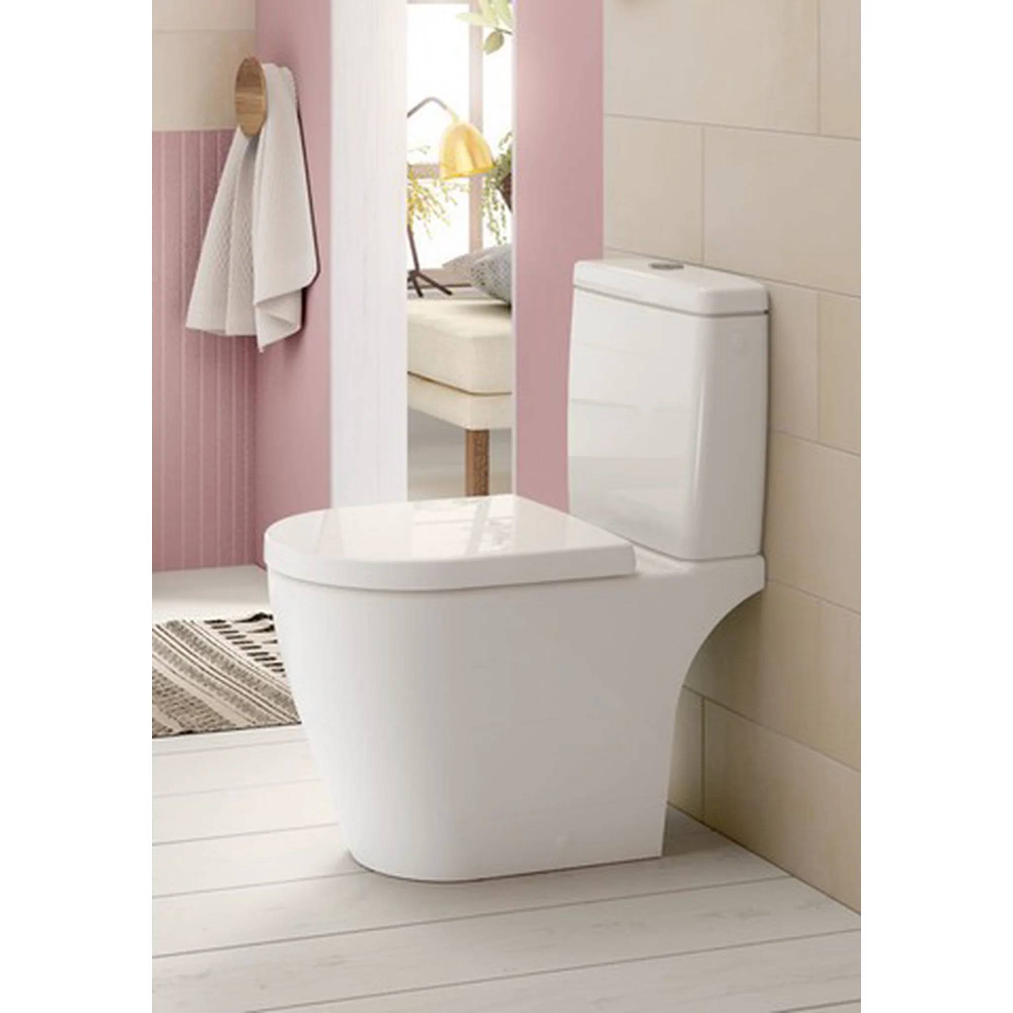 Eine moderne weiße Toilette in einem rosa-und-beige Badezimmer, gezeigt neben einem Wandspiegel und Handtuch, mit einem sauberen minimalistischen Design.