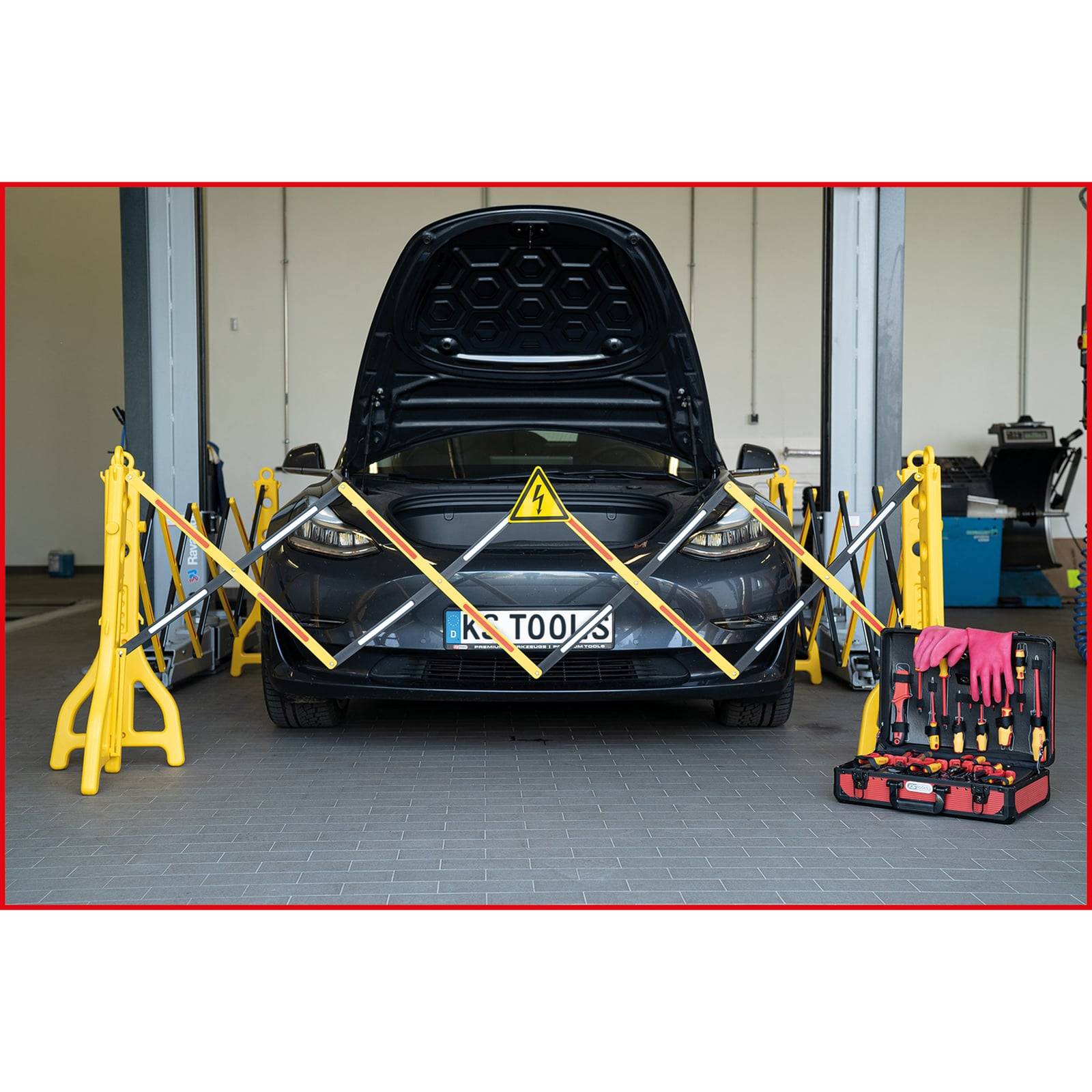 Ein Elektroauto mit geöffneter Motorhaube ist für Wartungsarbeiten abgesperrt. Ein gelbes Warnschild auf der Motorhaube, Werkzeuge und Sicherheitshandschuhe befinden sich in der Nähe.