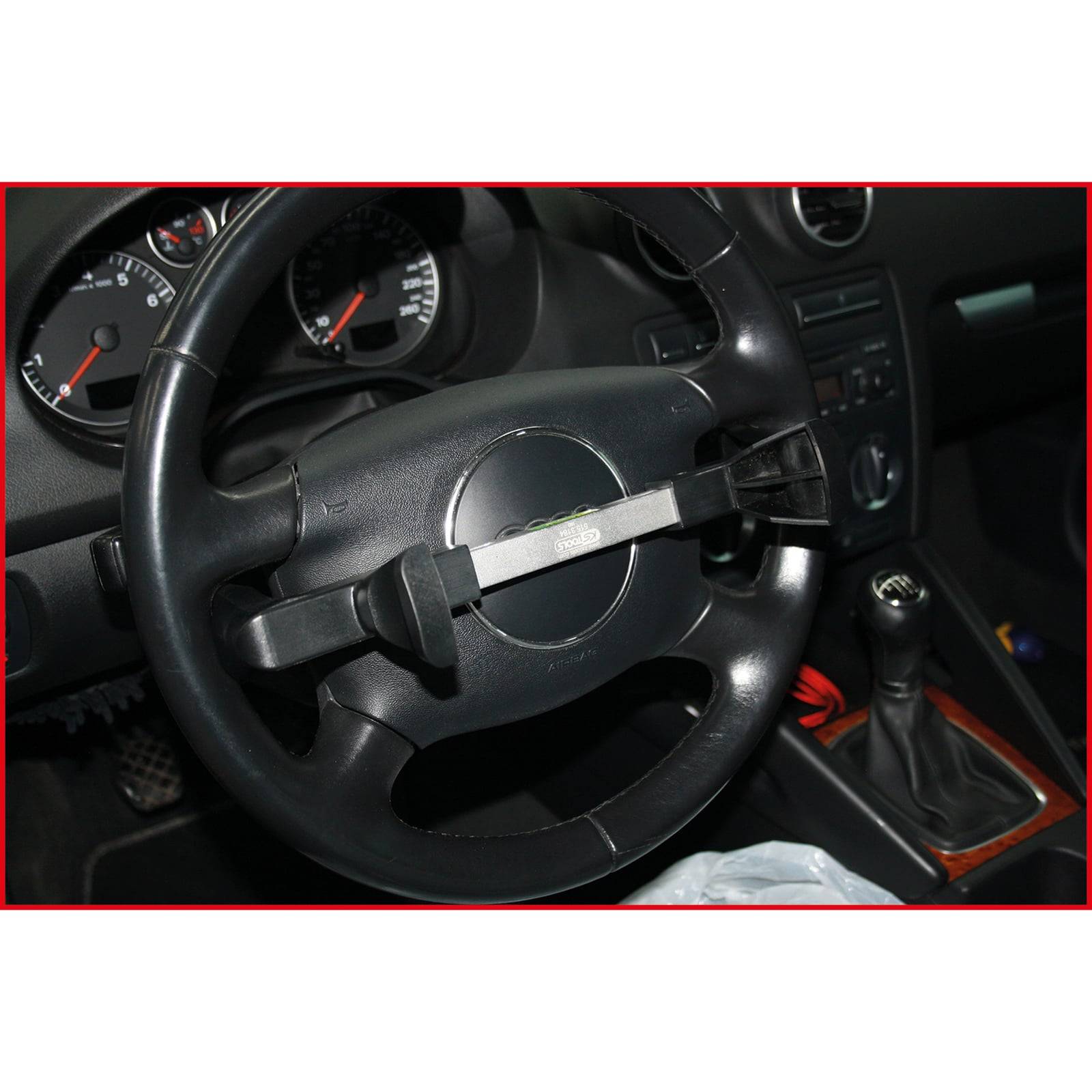Ein Lenkrad mit angebrachter Diebstahlschutzsperre, neben einem manuellen Schalthebel im Wageninneren. Tachometer im Hintergrund sichtbar.