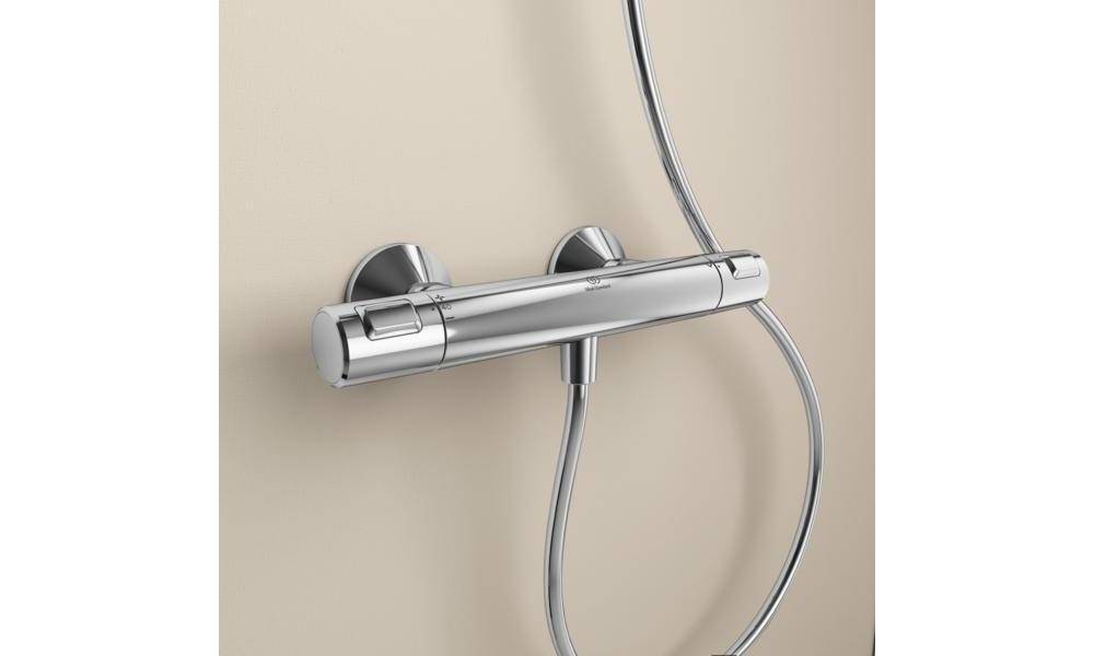 Chromglänzende Brausemischbatterie an einer beigen Wand montiert, mit angeschlossenem Schlauch und Duschleitung.