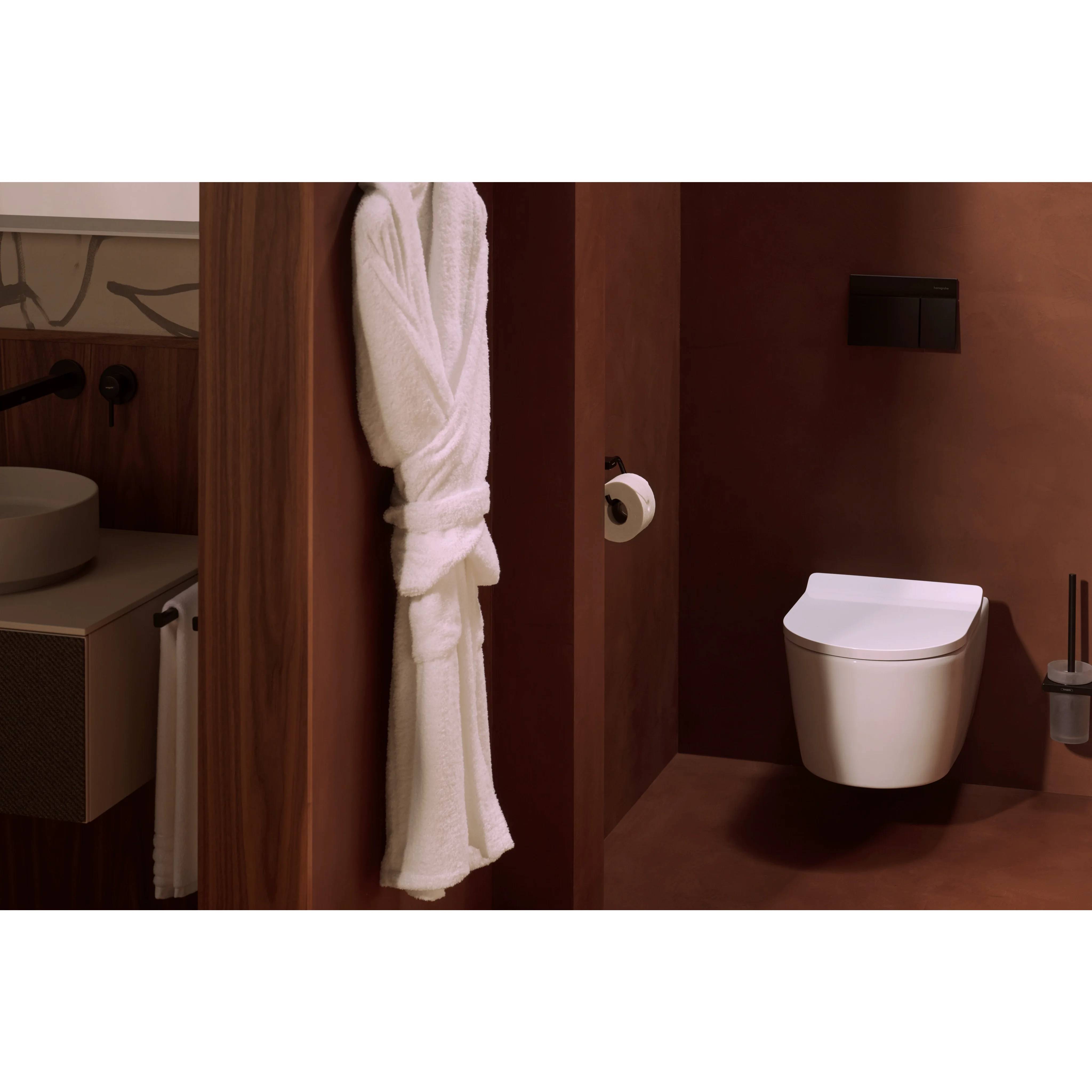 Modernes Badezimmer mit an der Wand montierter Toilette, Handtuch neben der Duschtrennwand hängend, und teilweise sichtbarem Waschbecken der Waschtischanlage.