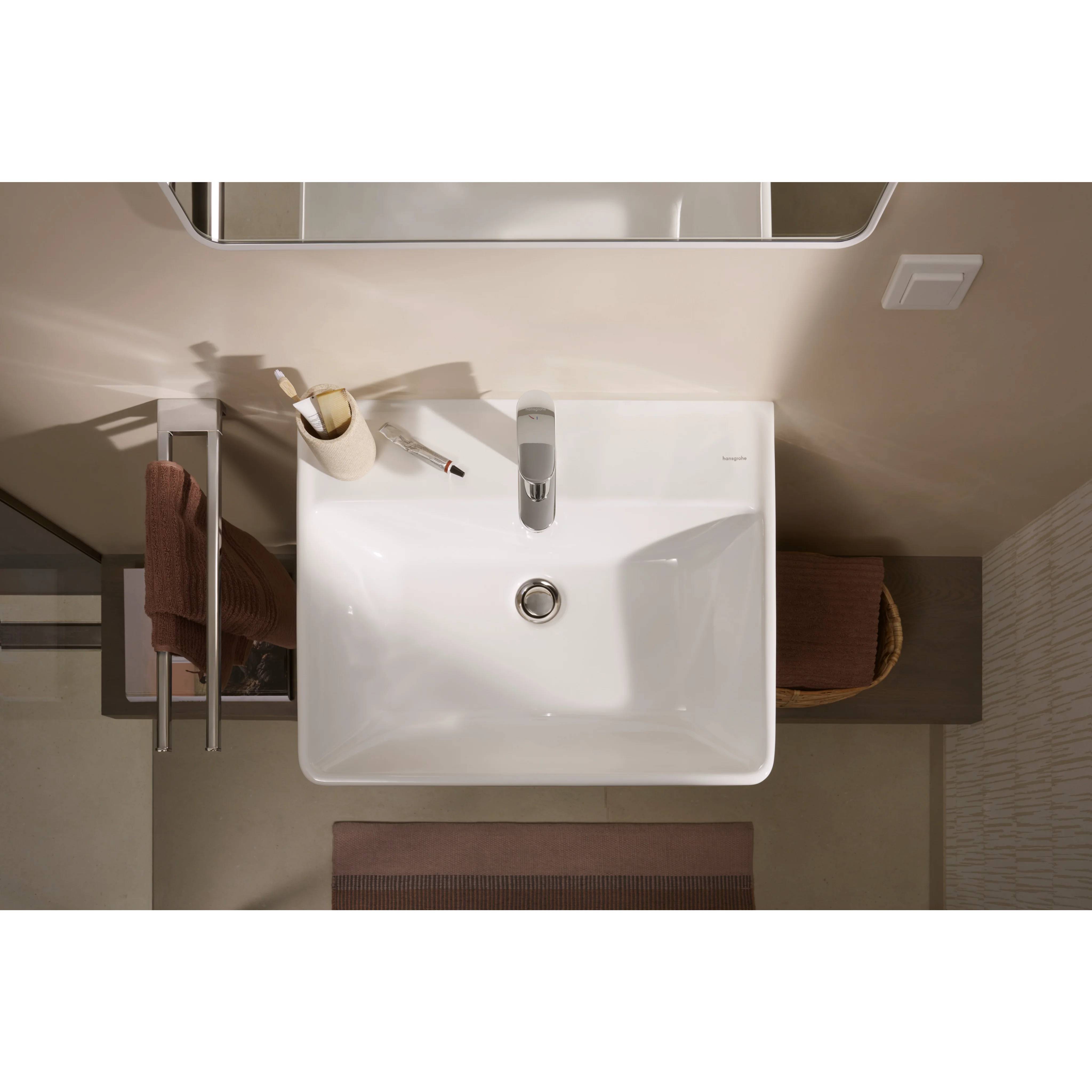 Draufsicht auf ein modernes Badezimmerbecken mit Wasserhahn, Seifenspender und Handtuch auf einem Waschtisch neben einem Spiegel.
