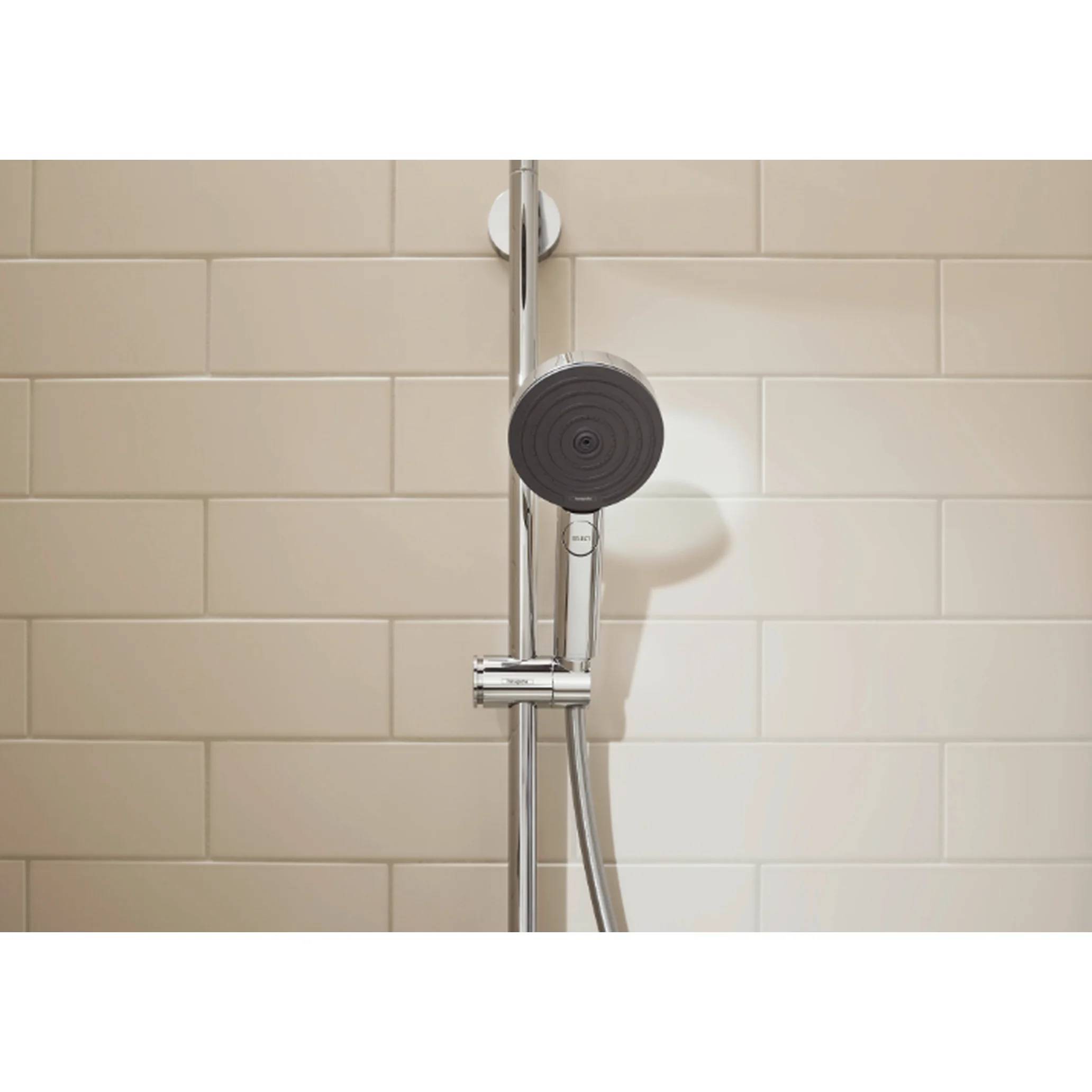 Chromdusche mit rundem Handbrauseaufsatz an beiger gekachelter Badezimmerwand, zentriert im Badezimmer.