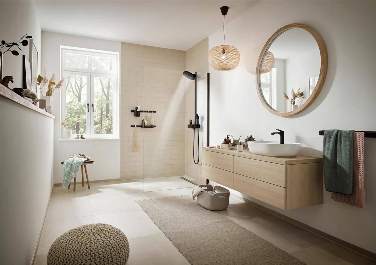 Modernes Badezimmer mit schwebendem Holzwaschtisch, rundem Spiegel, begehbarer Dusche, Fenster, Teppich und Handtüchern in hellem, neutralem Innendesign.