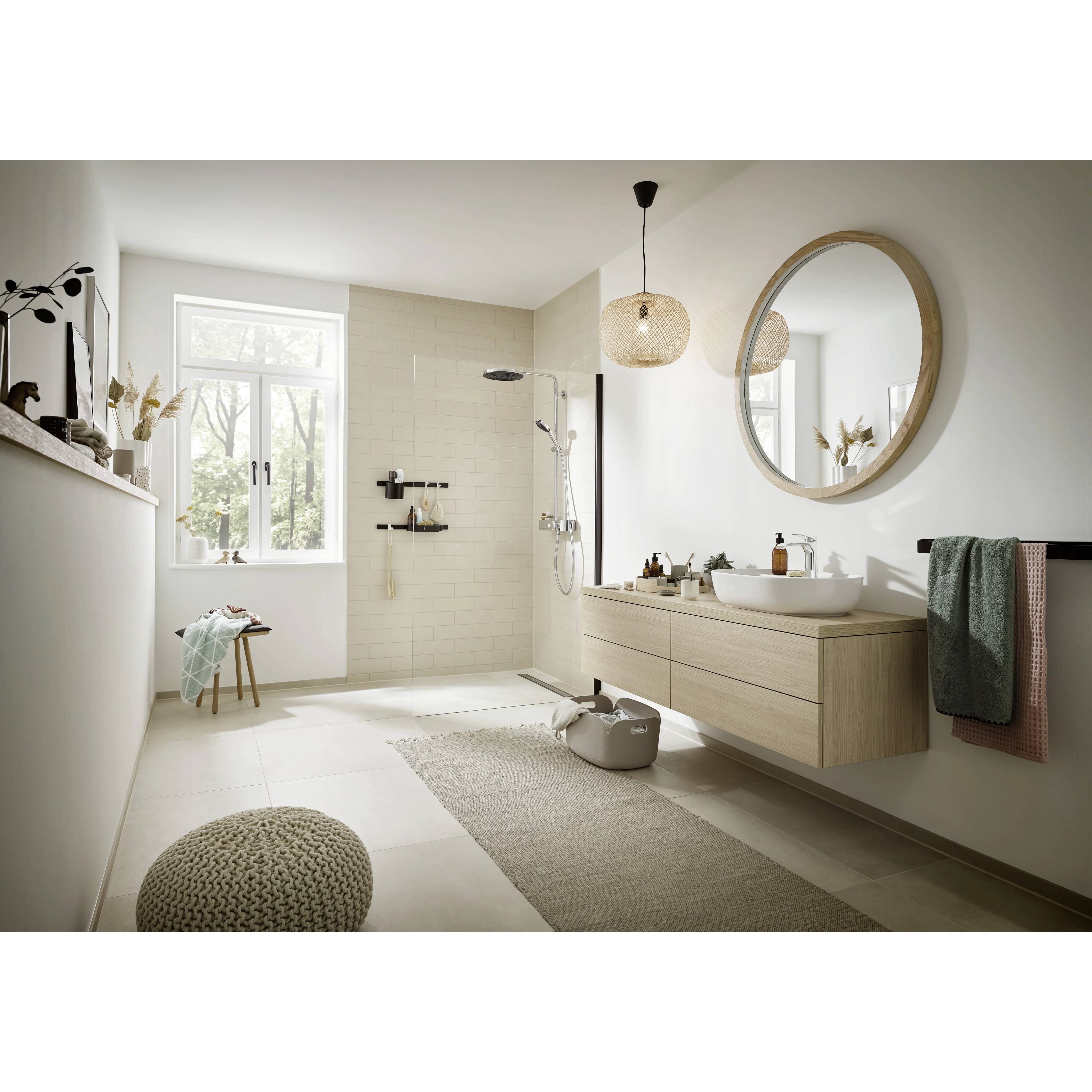 Helles modernes Badezimmer mit begehbarer Dusche, schwebendem Waschtisch, rundem Spiegel, Fenster und neutraler beiger Einrichtung.