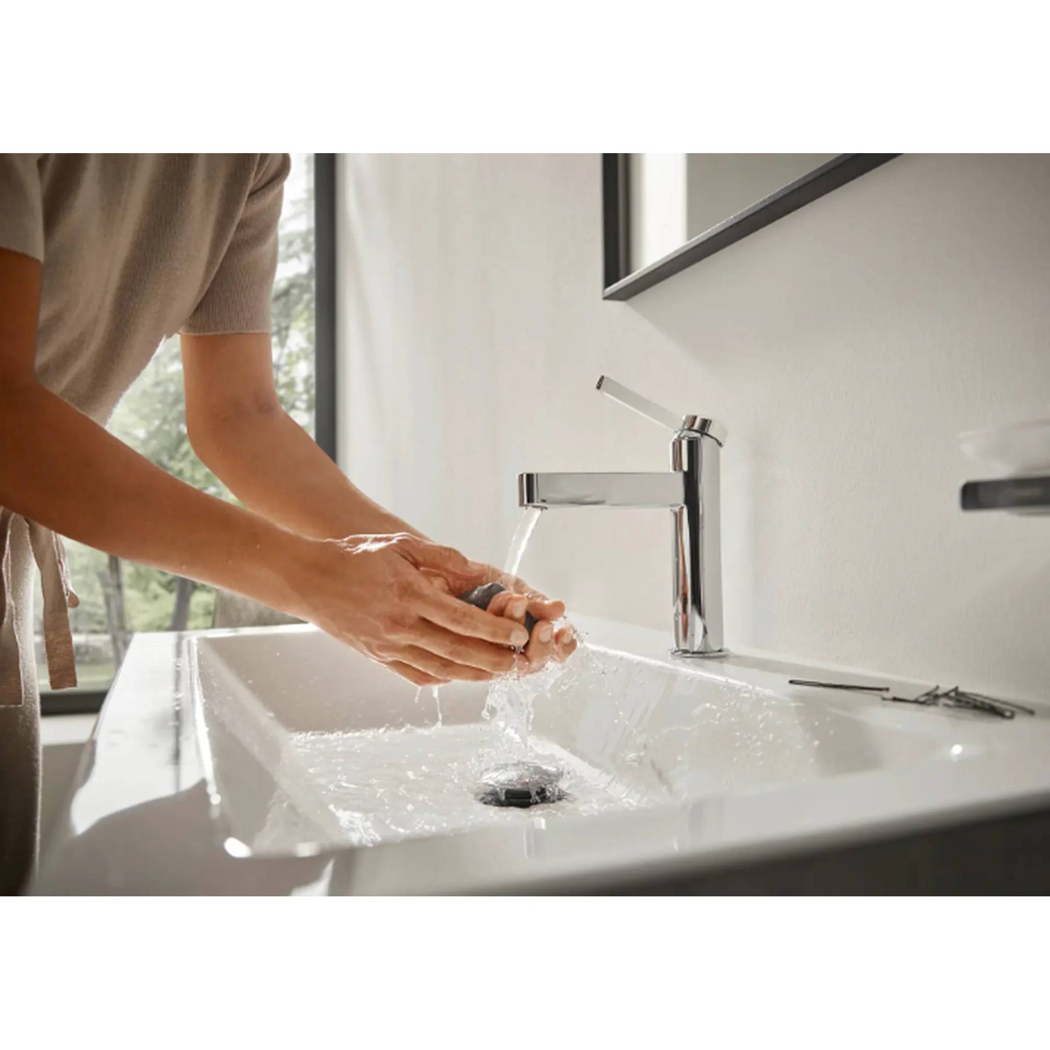 Person wäscht Hände unter fließendem Wasser an einem Waschbecken im Badezimmer.