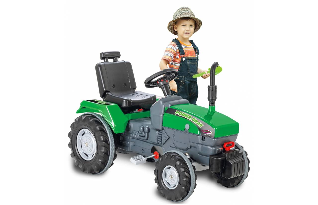 Kleines Kind steht neben einem grünen Spielzeugtraktor auf weißem Hintergrund, lächelt und hält das Lenkrad.