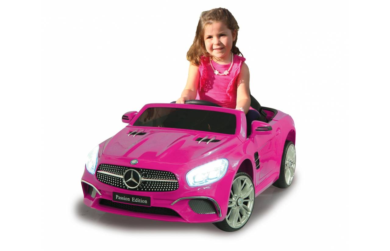 Kleines Mädchen, das in einem rosa Spielzeug-Mercedes-ähnlichen Cabriolet auf weißem Hintergrund sitzt.