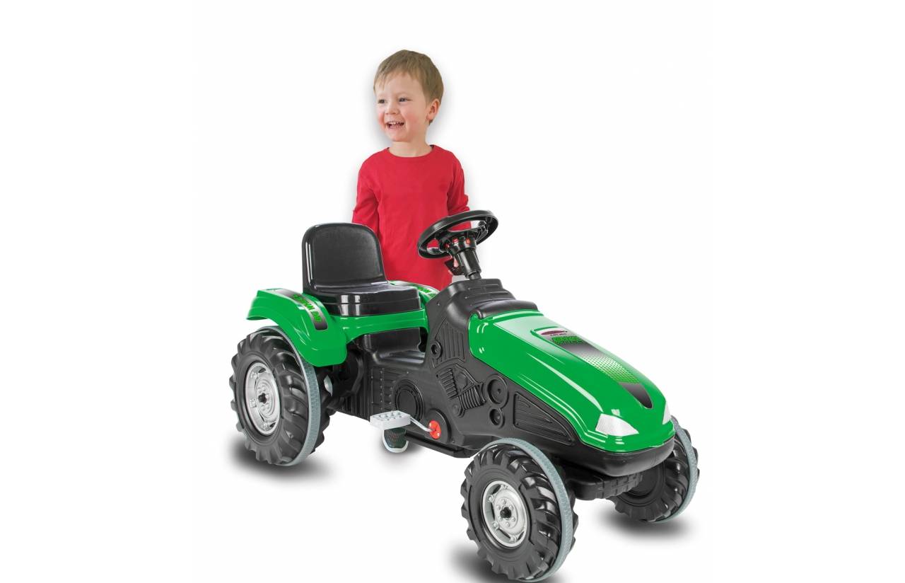 Kleines Kind, das hinter einem grünen Trettraktor auf weißem Hintergrund steht und lächelt