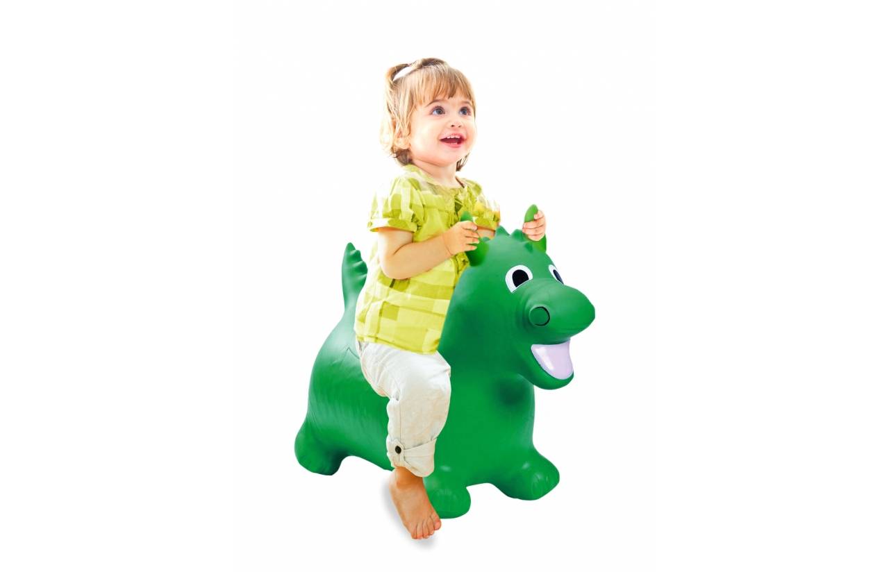 Kleines Kind auf einem grünen aufblasbaren Dinosaurier-Spielzeug auf weißem Hintergrund reitend, lächelnd und mit beiden Händen haltend.
