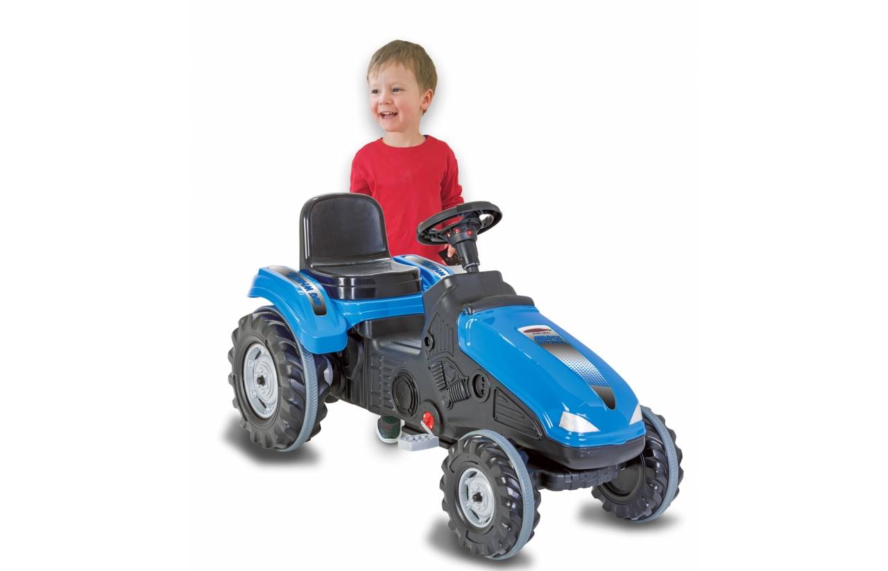 Ein kleiner Junge in einem roten Hemd steht hinter einem blauen Spielzeug-Trettraktor auf weißem Hintergrund.
