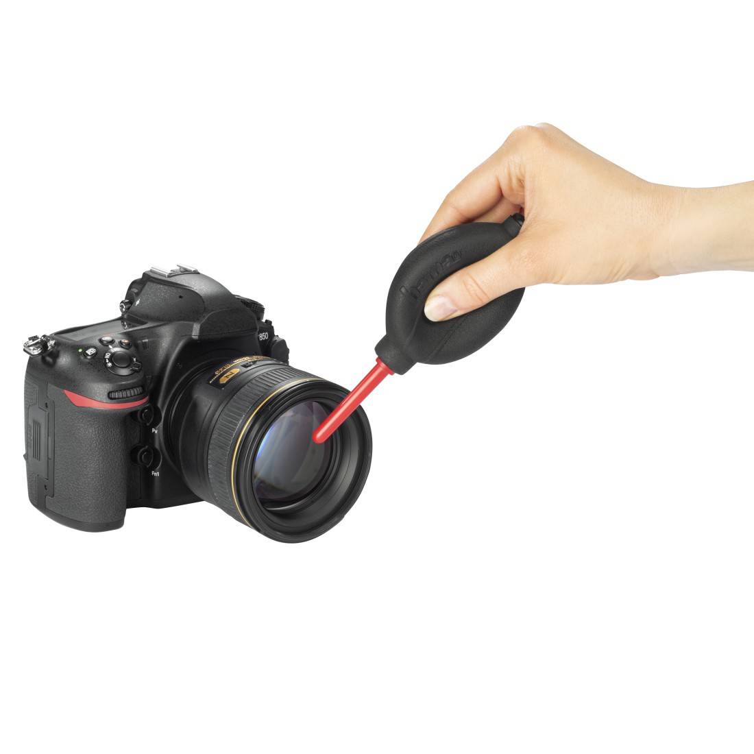 Eine Hand benutzt ein Luftgebläse mit einer roten Düse, um die Linse einer DSLR-Kamera zu reinigen.