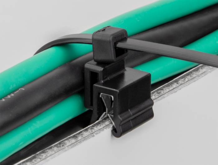 Schwarze Kabelklemme sichert mehrere grüne und schwarze Kabel gegen eine Oberfläche.