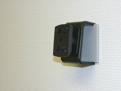 Wandmontierte schwarzgraue Elektrosteckdostenabdeckung oder Steckeradapter auf einer strukturierten weißen Oberfläche.