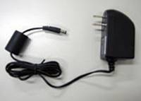Schwarzer AC-Stromadapter mit Kabel und zweipoliger Steckdose auf einer hellen Oberfläche liegend.