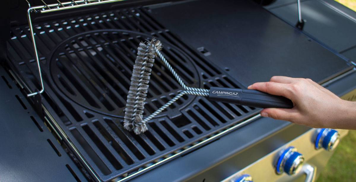 Mit einer Drahtbürste von Hand ein Gasgrill-Rost reinigen.