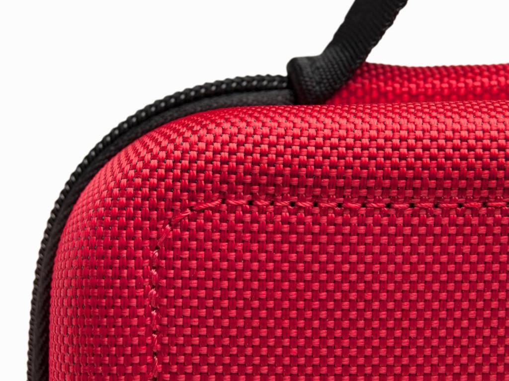 Nahaufnahme einer roten strukturierten Stoff-Tasche oder eines Koffers mit schwarzem Reißverschluss und Riemen auf weißem Hintergrund.