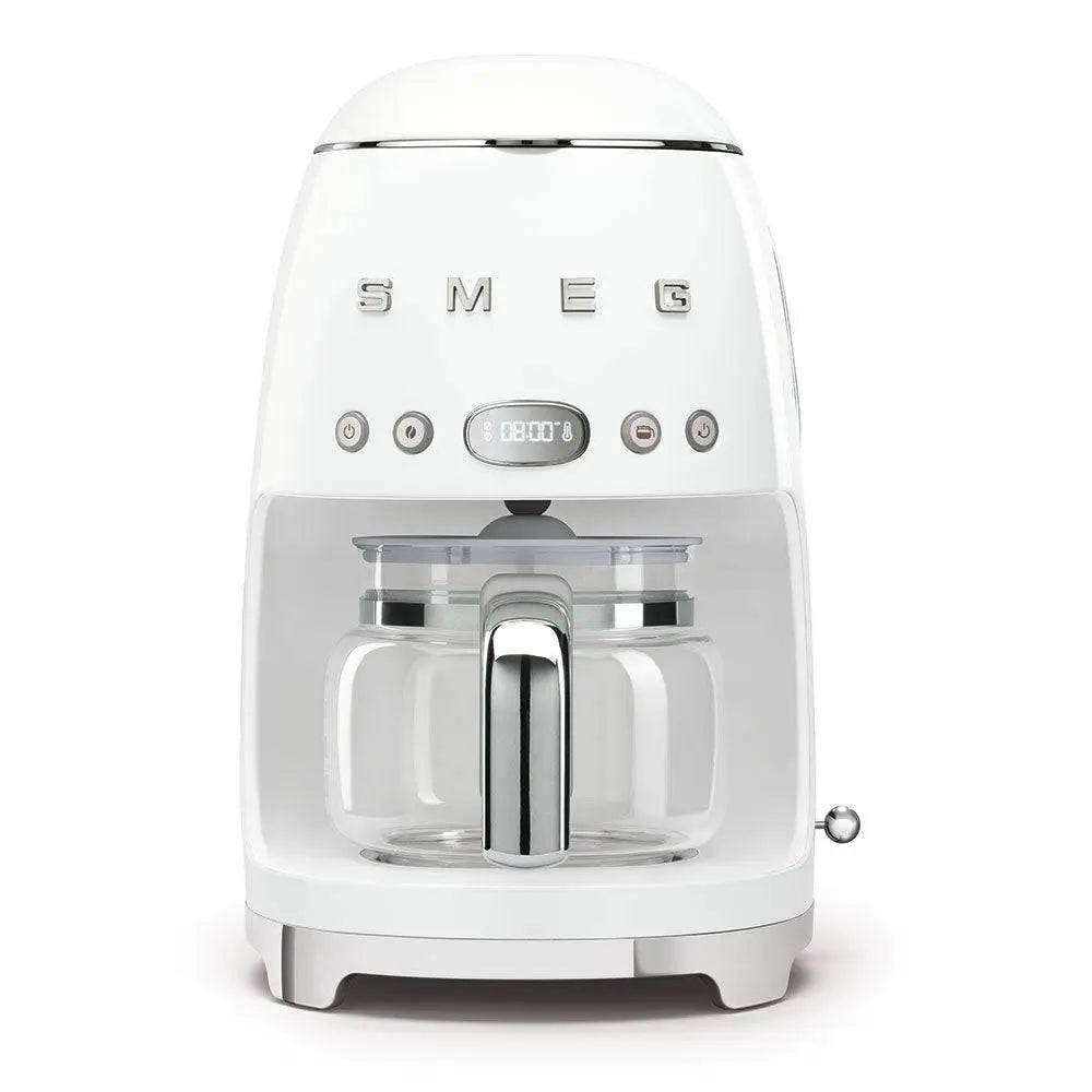 Weiße SMEG-Arbeitsplatten-Kaffeemaschine mit Glaskanne, Frontbedienung und digitales Display auf neutralem Hintergrund.