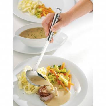 Hand serviert cremige Sauce über einem plattierten Gericht aus Pasta, Gemüse und einem gebratenen Medaillon, mit Suppe im Hintergrund.