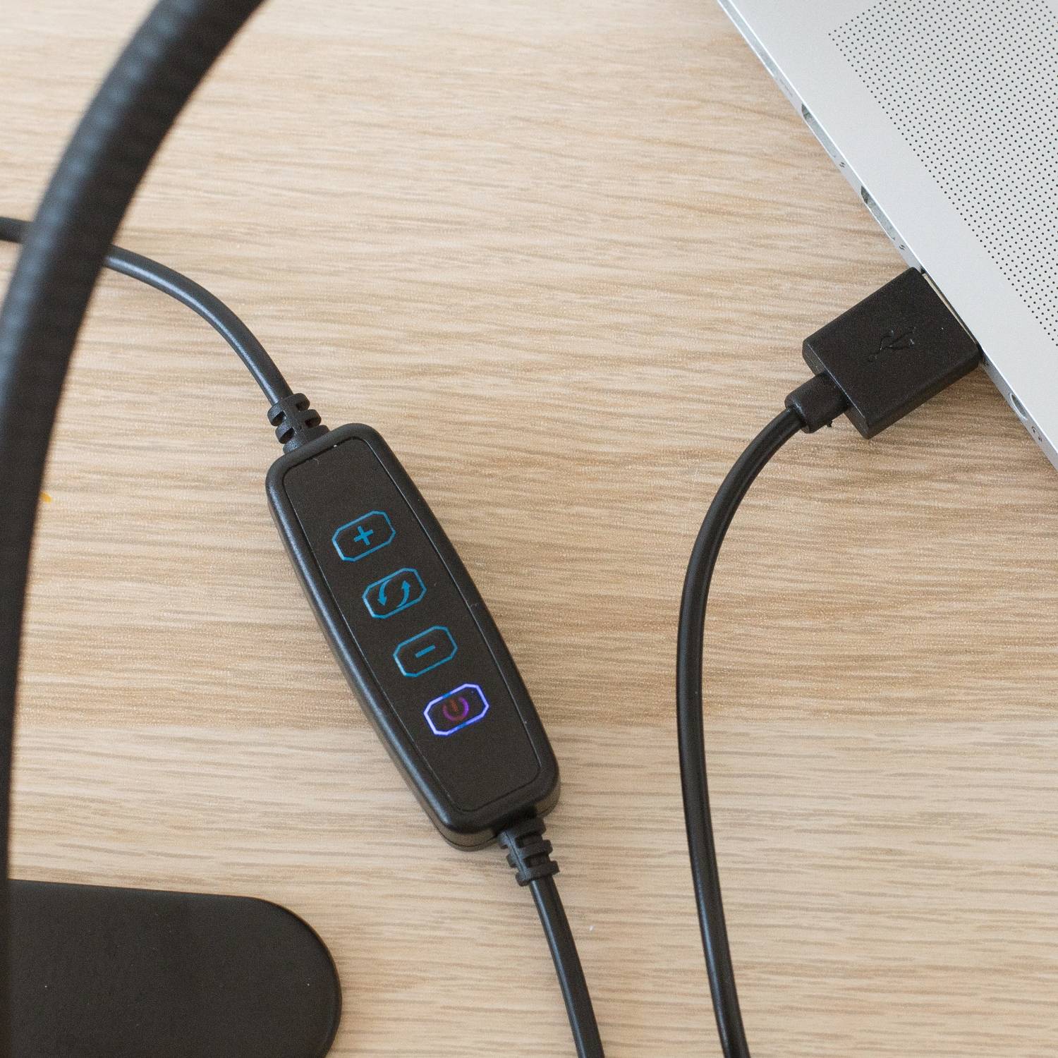 USB-Kabel mit integrierten Steuertasten, das mit einem Laptop auf einem Holzschreibtisch verbunden ist.