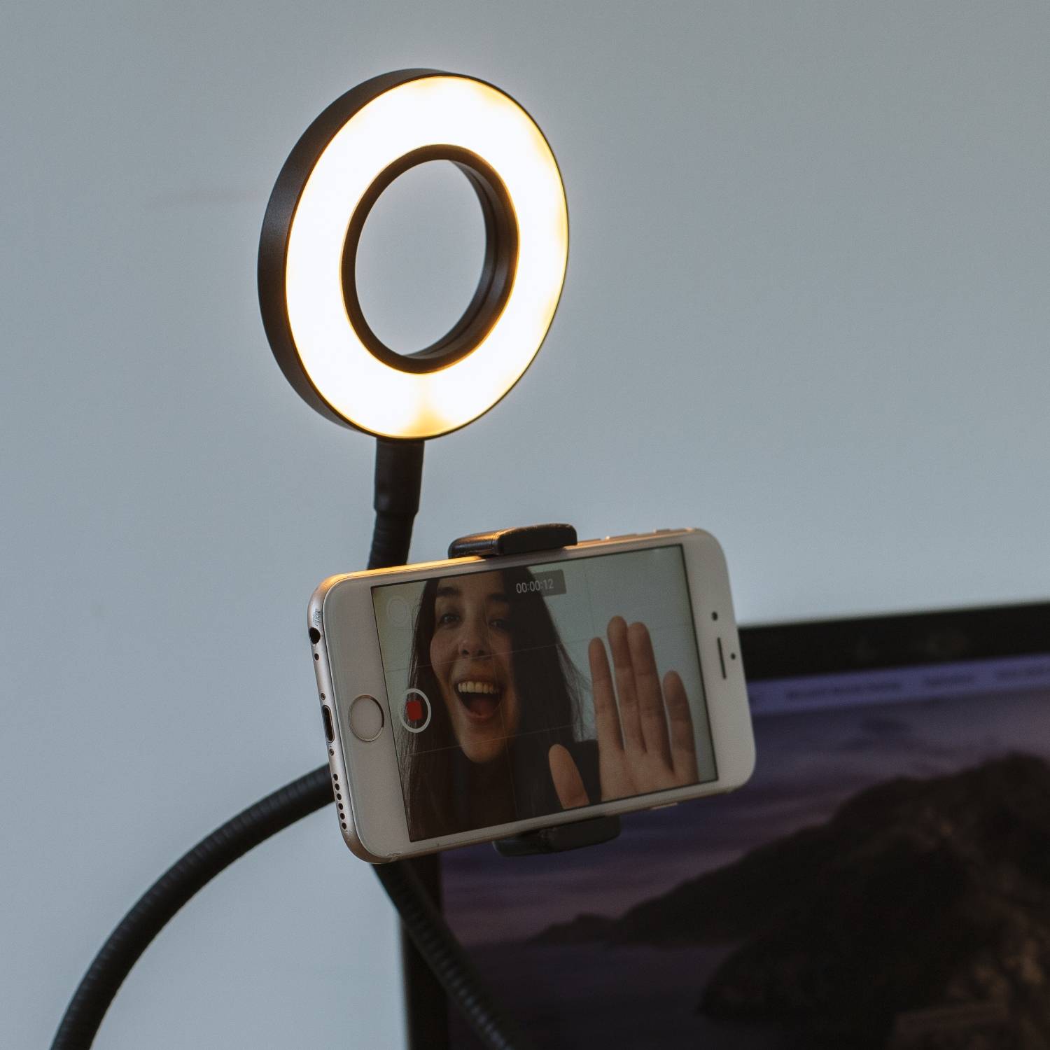Smartphone auf einem Ringlicht-Stativ montiert, das eine Frau in einem Videoanruf zeigt, die in die Kamera winkt.