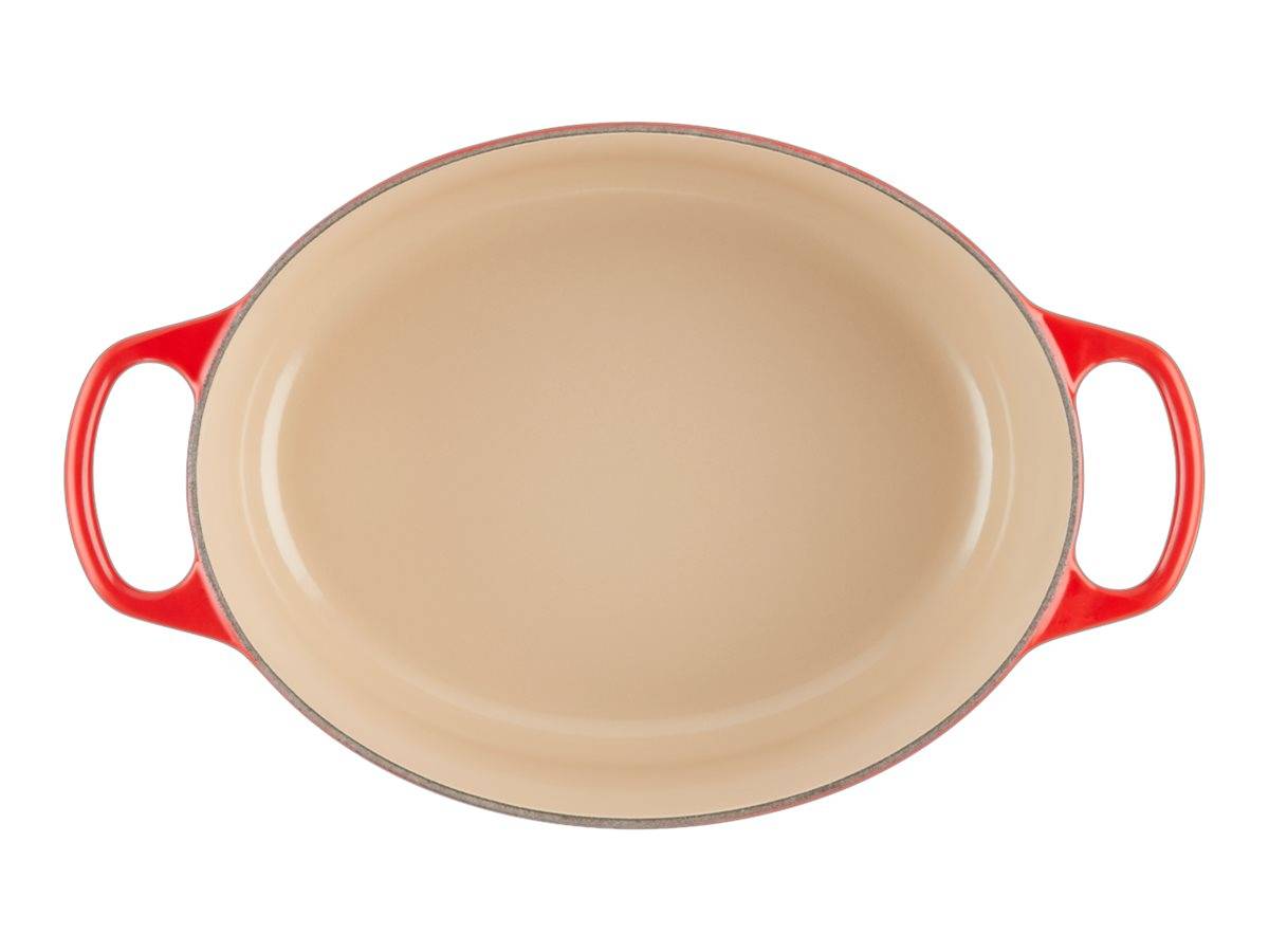 Ovale Backform mit rotem Griff aus Keramik mit beigem Innenbereich, leer auf weißem Hintergrund abgebildet.