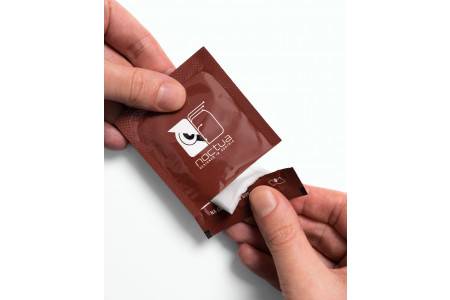 Hände, die ein braunes Papiertüten-Päckchen öffnen, das ein weißes Tuch oder Taschentuch darin enthüllt.