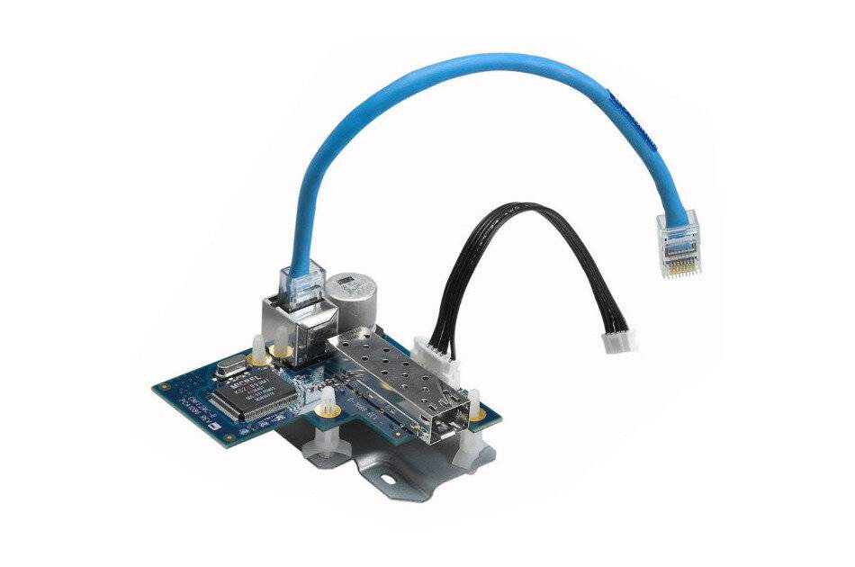 Kleine Leiterplatte mit einem Metallmodul und angeschlossenem blauem Ethernet-Kabel, mit einem lose angebrachten schwarzen Stecker auf weißem Hintergrund.
