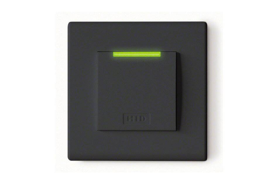 Schwarzes, an der Wand montiertes quadratisches Gerät mit einem zentrierten Schalter und einer leuchtenden grünen Anzeigelampe oben.