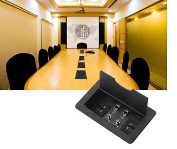 Ein langer Konferenzraum mit einem Holztisch, Stühlen und einer Projektionsleinwand, die ein buntes Diagramm zeigt. Einblendung zeigt Tischanschlüsse.