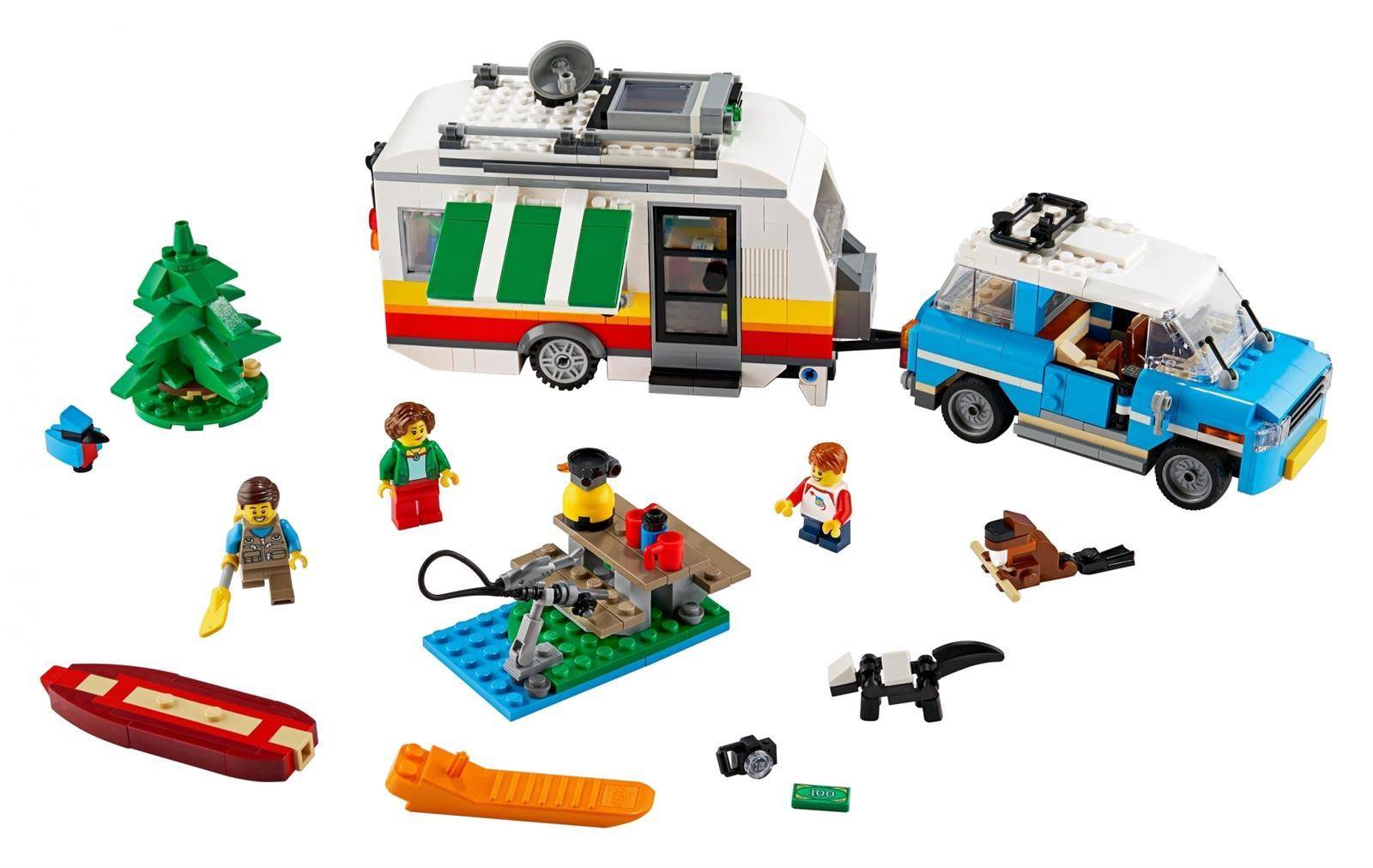 LEGO-Campingszene mit einem Wohnmobil, blauem Geländewagen, Kanu, kleinem Lagerfeuer auf einer Basis, Baum und mehreren Minifiguren mit Outdoor-Ausrüstung.