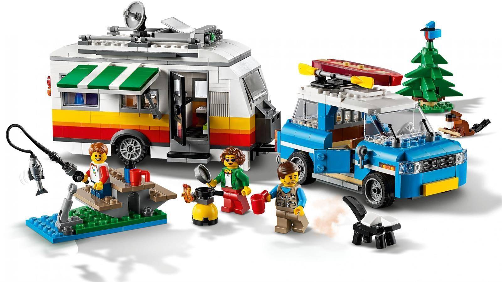LEGO-Campingszene mit einem gestreiften Wohnmobil, einem blauen Pickup mit Kanu und Baum sowie Minifiguren, die einen Campingplatz mit Tisch und Grill aufbauen.
